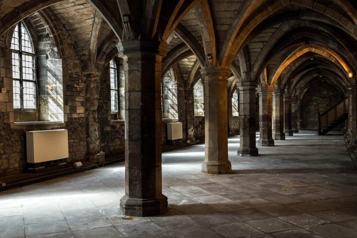 Picture of the undercroft at Greyfriars. Stone pillars holding up a vaulted ceiling with a row of windows along the far wall.